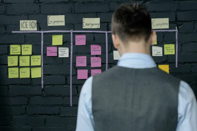 Une personne devant un panneau de suivi de projet à base de post-its sur un mur sombre. Business plan et roadmap.